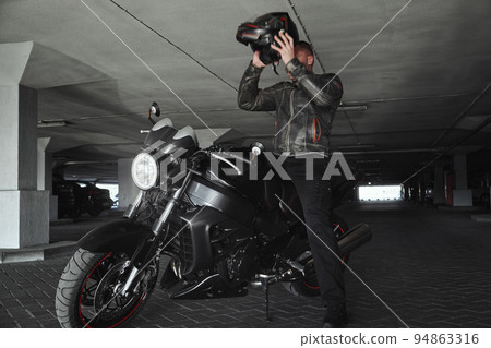 A man sitting on a motorcycle takes off his helmet in underground parking garage, in motion 94863316
