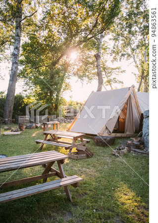 Countryside camping. Nature relax. Orchard stuff. Cozy canvas tent with picnic eating zone on sunshine yard outdoor. Countryside camping. Nature relax. Orchard stuff. Cozy canvas tent with picnic eating zone on sunshine yard outdoor. 94863561