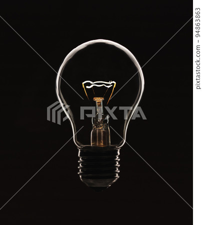 A glowing electric light bulb in a counter light on a black background A glowing electric light bulb in a counter light on a black background 94863863