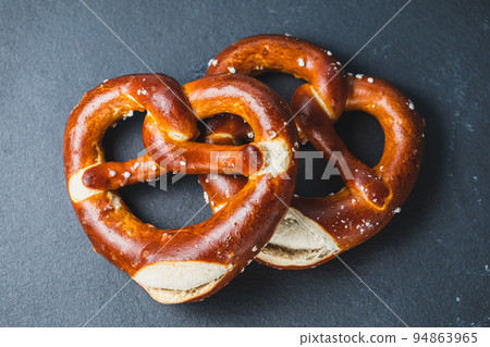 Two homemade freshly baked soft pretzels on black backround. Traditional Bavarian pretzel for Octoberfest. Top view, copy space Two homemade freshly baked soft pretzels on black backround. Traditional Bavarian pretzel for Octoberfest. Top view, copy space 94863965