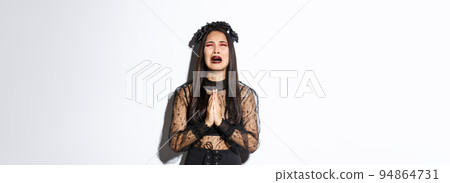 Miserable young asian woman in trouble pleading god, crying and begging for help, wearing halloween gothic dress and wreath, supplicating over white background Miserable young asian woman in trouble pleading god, crying and begging for help, wearing halloween gothic dress and wreath, supplicating over white background 94864731