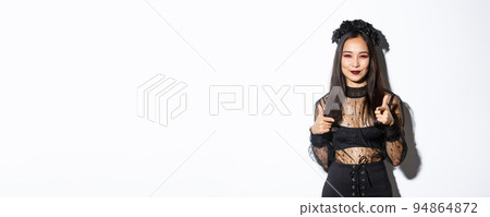 Cheeky and happy attractive woman in witch outfit pointing fingers at camera and smiling, making compliment or praising something good, standing in halloween costume over white background Cheeky and happy attractive woman in witch outfit pointing fingers at camera and smiling, making compliment or praising something good, standing in halloween costume over white background 94864872
