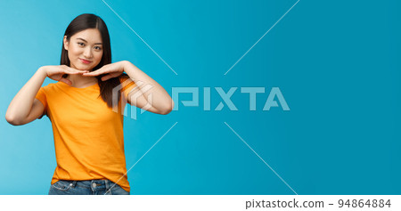 Sweet lovely tender asian girl brunette, tilt head smiling show clean pure face hold palms under jawline satisfied after applying skincare product stand blue background wear yellow t-shirt Sweet lovely tender asian girl brunette, tilt head smiling show clean pure face hold palms under jawline satisfied after applying skincare product stand blue background wear yellow t-shirt 94864884