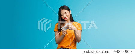 Cute entertained good-looking urban female student spend break playing racing game, hold smartphone horizontal tilt phone move car, smiling broadly standing enthusiastic blue background Cute entertained good-looking urban female student spend break playing racing game, hold smartphone horizontal tilt phone move car, smiling broadly standing enthusiastic blue background 94864900