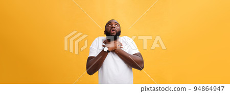 Portrait of african american man with hands raised in shock and disbelief. Isolated over yellow background. Portrait of african american man with hands raised in shock and disbelief. Isolated over yellow background. 94864947