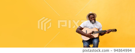 Handsome african american retro styled guitarist playing acoustic guitar isolated on yellow background. 94864994