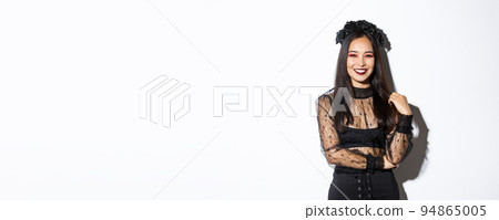 Beautiful young happy woman enjoying halloween party, smiling and looking cheerful while wearing her evil witch costume for trick or treating, standing over white background 94865005
