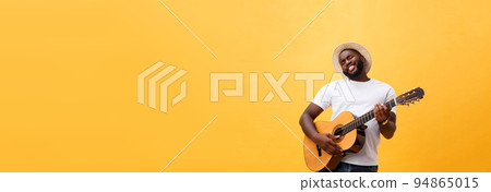 Muscular black man playing guitar, wearing jeans and white tank-top. Isolate over yellow background. Muscular black man playing guitar, wearing jeans and white tank-top. Isolate over yellow background. 94865015