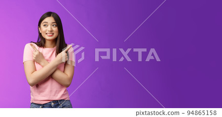 Cheerful timid cute asian girl, look tender, smiling gazing aside cross hands chest, pointing sideways, show left right, making decision, gathering confidence choose, purple background 94865158