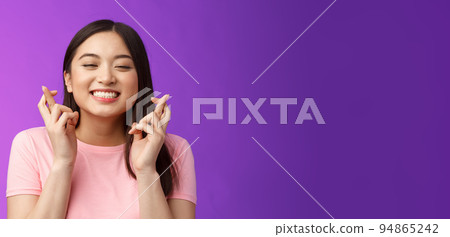 Headshot dreamy lucky cute asian girl believe she win, make wish, cross fingers good fortune, close eyes smiling happily feeling hopeful receive positive results, stand purple background 94865242