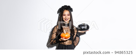 Image of attractive korean girl celebrating halloween in gothic lace dress, impersonating witch and holding two pumpkins Image of attractive korean girl celebrating halloween in gothic lace dress, impersonating witch and holding two pumpkins 94865325