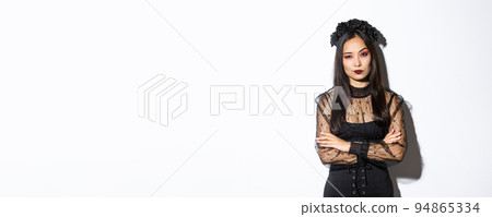 Skeptical and unamused asian woman dressed in halloween costume looking disappointed at camera, cross arms chest. Female in black gothic dress and wreath judging someone Skeptical and unamused asian woman dressed in halloween costume looking disappointed at camera, cross arms chest. Female in black gothic dress and wreath judging someone 94865334