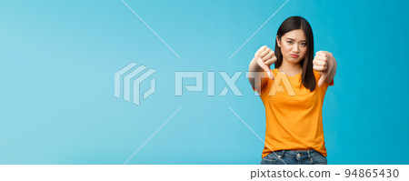 Upset gloomy asian girl with dark haircut frowning sulking sad, disappointed, show thumbs-down grimacing, give negative opinion, judging bad uninteresting movie, stand blue background Upset gloomy asian girl with dark haircut frowning sulking sad, disappointed, show thumbs-down grimacing, give negative opinion, judging bad uninteresting movie, stand blue background 94865430