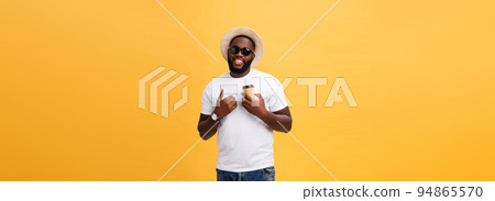 Stylish young african american man holding cup of take away coffee isolated over yellow background. Stylish young african american man holding cup of take away coffee isolated over yellow background. 94865570