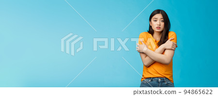 Girl feeling uncomfortable walking light yellow t-shirt, hugging herself trembling, shaking feeling cold, freezing windy weather, frowning grimacing discomfort, stand blue background Girl feeling uncomfortable walking light yellow t-shirt, hugging herself trembling, shaking feeling cold, freezing windy weather, frowning grimacing discomfort, stand blue background 94865622