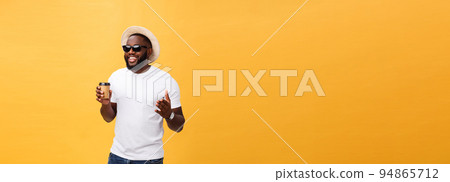 Stylish young african american man holding cup of take away coffee isolated over yellow background. 94865712