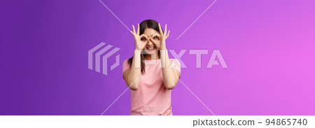 Cheerful friendly carefree asian woman having fun fool around, show okay ok signs on eyes make glasses from fingers, smiling delighted, mimicking funny emotions, stand purple background happy 94865740