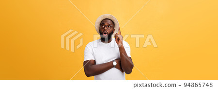 Portrait of a pensive afro american man in glasses looking up at copyspace isolated on a yellow background 94865748