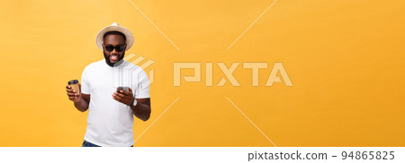 Handsome African American with mobile phone and take away coffee cup. Isolated over yellow gold background. 94865825