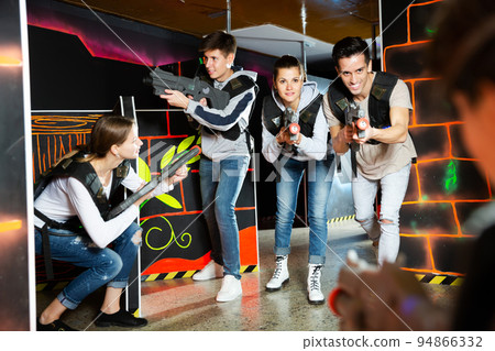 Ordinary Laser tag players young mens and womens playing in teams in dark laser tag station Ordinary Laser tag players young mens and womens playing in teams in dark laser tag station 94866332