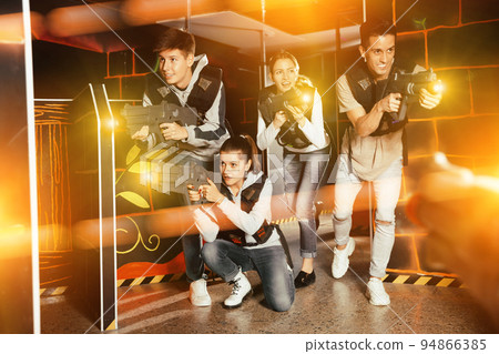 Excited young people playing enthusiastically laser tag game two teams opposite each other in dark room 94866385