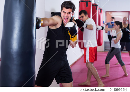 enthusiastic sportsman in the boxing hall practicing boxing punches with boxing bag 94866664