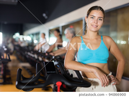 Woman posing near stationary bike in gym Woman posing near stationary bike in gym 94866900