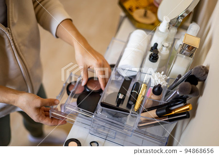 Closeup female hands putting luxury cosmetic into acrylic box with drawer storage organization Closeup female hands putting luxury cosmetic into acrylic box with drawer storage organization 94868656