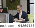 A European adult man with a beard works at a computer in the office of company 94869328