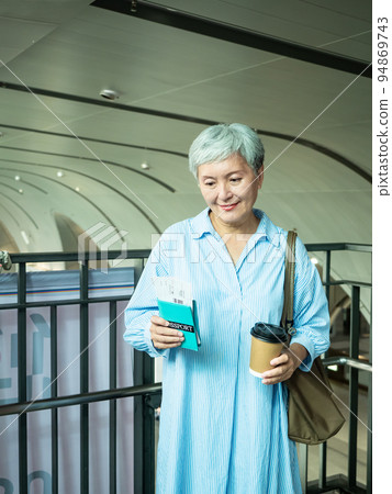 Portrait of happy senior adult elderly asia woman 60s holding passport and paper cup, drinking coffee for travel concept. 94869743