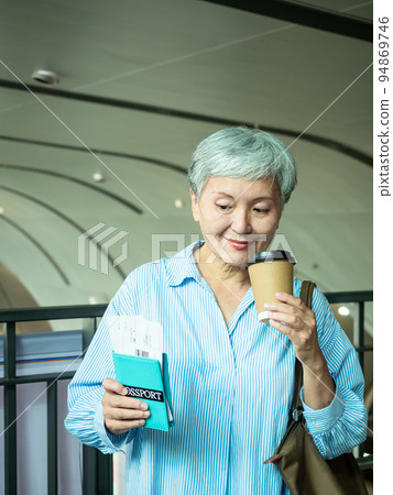 Portrait of happy senior adult elderly asia woman 60s holding passport and paper cup, drinking coffee for travel concept. 94869746