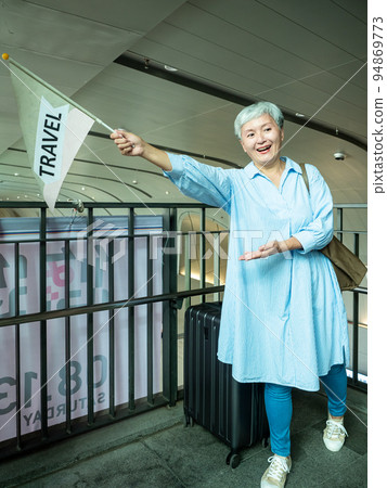 Portrait of senior adult elderly asian woman 60s smiling standing with suitcase luggage bag and holding guided flag pole for travel concept. Portrait of senior adult elderly asian woman 60s smiling standing with suitcase luggage bag and holding guided flag pole for travel concept. 94869773