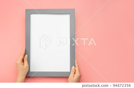 Hanging a photo frame mockup on pink wall. Picture frame mockup. Holding frame mockup. Photo Mockup. Female hands hold frame with white paper. copy space 94872356