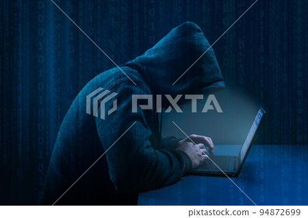 Hacker. Hacker using laptop on dark binary code digital background. Faceless hooded anonymous computer hacker. Hacking and malware concept. 94872699