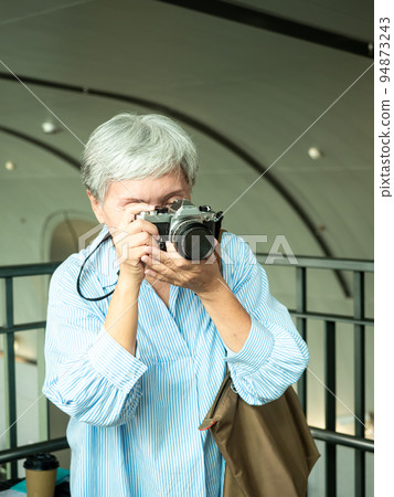 60 多歲的亞洲女性揮舞著單眼觀察機或底部單相機,旅行或觀光探索概念。 60 多歲的亞洲女性揮舞著單眼觀察機或底部單相機,旅行或觀光探索概念。 94873243