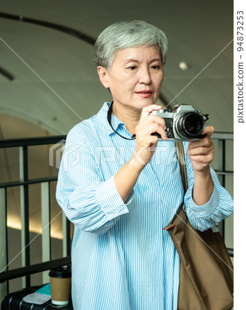 60 多歲的亞洲女性揮舞著單眼觀察機或底部單相機,旅行或觀光探索概念。 60 多歲的亞洲女性揮舞著單眼觀察機或底部單相機,旅行或觀光探索概念。 94873253