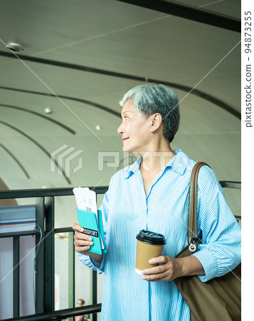 一位 60 歲的亞洲成熟女性戴著紙杯喝茶或喝咖啡,等待旅行或觀光的概念。 一位 60 歲的亞洲成熟女性戴著紙杯喝茶或喝咖啡,等待旅行或觀光的概念。 94873255