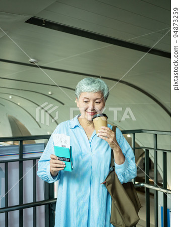 A 60-year-old mature Asian woman wears a paper cup for tea or coffee, and the concept of waiting for travel or sightseeing. 94873259