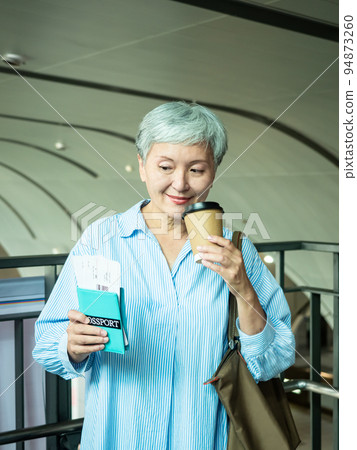 A 60-year-old mature Asian woman wears a paper cup for tea or coffee, and the concept of waiting for travel or sightseeing. 94873260