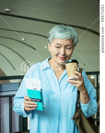 一位 60 歲的亞洲成熟女性戴著紙杯喝茶或喝咖啡，等待旅行或觀光的概念。 94873262