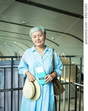 60多歲的亞洲熟年婦女微笑著站著,身旁有手提箱行李袋和手持登機證與護照,適用於covid19疫情後旅 60多歲的亞洲熟年婦女微笑著站著,身旁有手提箱行李袋和手持登機證與護照,適用於covid19疫情後旅 94873263