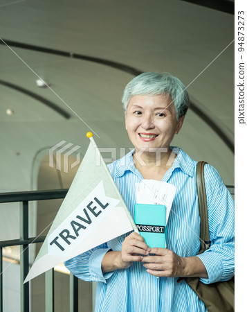 60歲亞洲老太婆畫像，微笑，駐紮手袋，提箱，手持旗桿，移動旅行樂隊的概念。 94873273