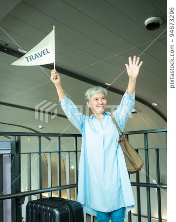 60歲亞洲老太婆畫像，微笑，駐紮手袋，提箱，手持旗桿，移動旅行樂隊的概念。 94873296