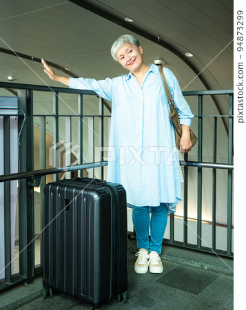 60多歲的亞洲熟年婦女微笑著站著,身旁有手提箱行李袋和手持登機證與護照,適用於covid19疫情後旅 94873299