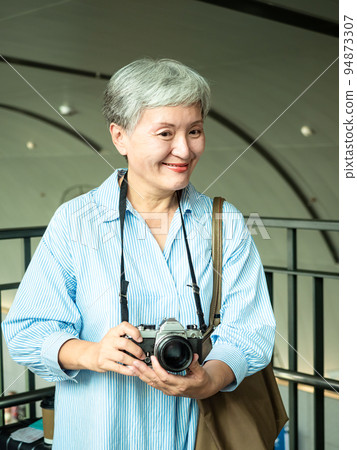 60 多歲的亞洲女性揮舞著單眼觀察機或底部單相機,旅行或觀光探索概念。 60 多歲的亞洲女性揮舞著單眼觀察機或底部單相機,旅行或觀光探索概念。 94873307