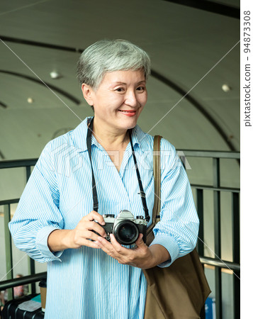 60 多歲的亞洲女性揮舞著單眼觀察機或底部單相機,旅行或觀光探索概念。 60 多歲的亞洲女性揮舞著單眼觀察機或底部單相機,旅行或觀光探索概念。 94873308