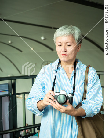 60 多歲的亞洲女性揮舞著單眼觀察機或底部單相機,旅行或觀光探索概念。 60 多歲的亞洲女性揮舞著單眼觀察機或底部單相機,旅行或觀光探索概念。 94873309