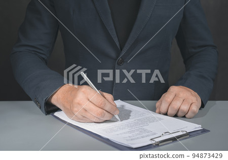 Businessman signs contract. Holding pen in hand. Businessman signing contract at table. Signing legal document. dark background 94873429