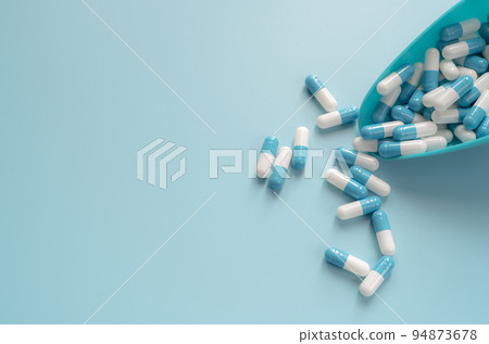 Blue and white capsules pill in plastic spoon and on blue background. Antibiotics drug resistance. Antimicrobial capsule pills. Pharmaceutical industry. Pharmacy drugstore products. Pharmaceutics. 94873678