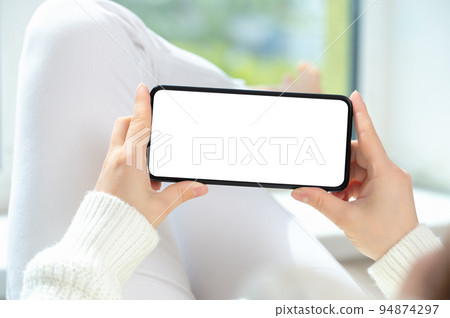 Woman lies in relaxed position and watches video content on cellphone or mobile smartphone. holding phone horizontally Woman lies in relaxed position and watches video content on cellphone or mobile smartphone. holding phone horizontally 94874297